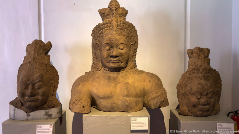 Three monumental stone heads displayed together, including an elaborately crowned central head.