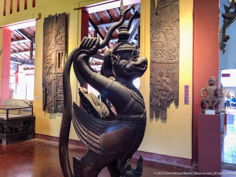 Bronze Garuda lifting an entwined naga above his head with wings spread.