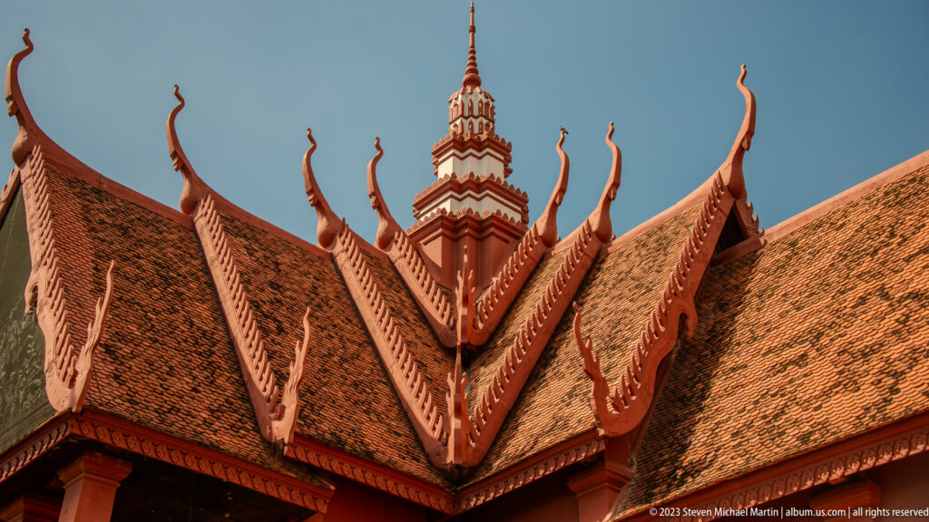 Layered red museum roofs with curling finials and a tall central tower silhouetted against blue sky.