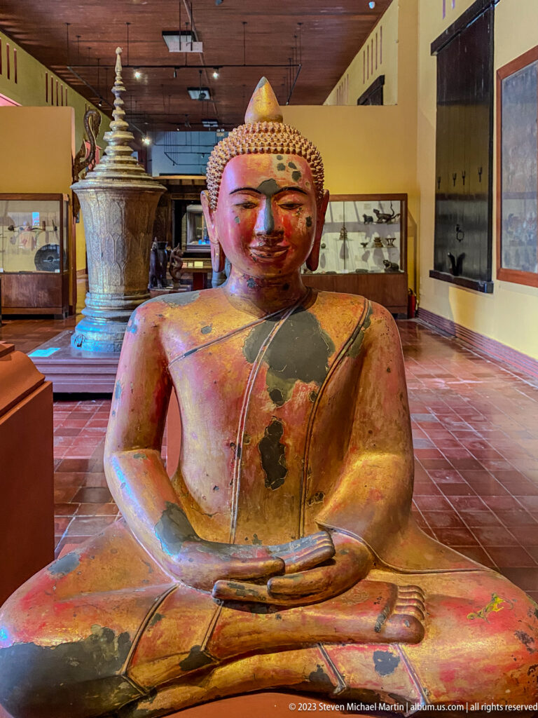 Seated Buddha retaining patches of red, gold, and black lacquer across body and robe.