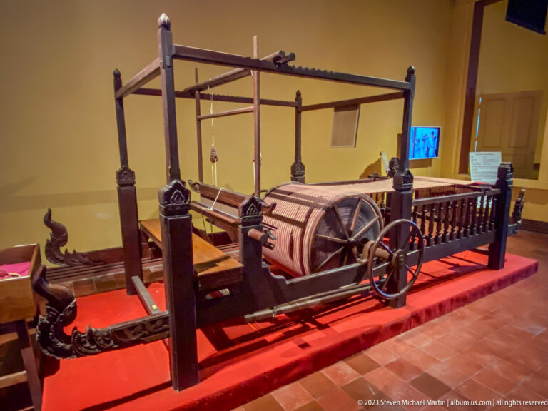 Large traditional wooden loom with rollers, frame, heddles, and weaving mechanisms clearly visible.