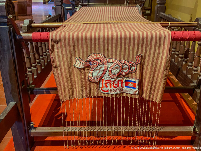 Striped Cambodian krama stretched across a traditional loom with unfinished threads visible.