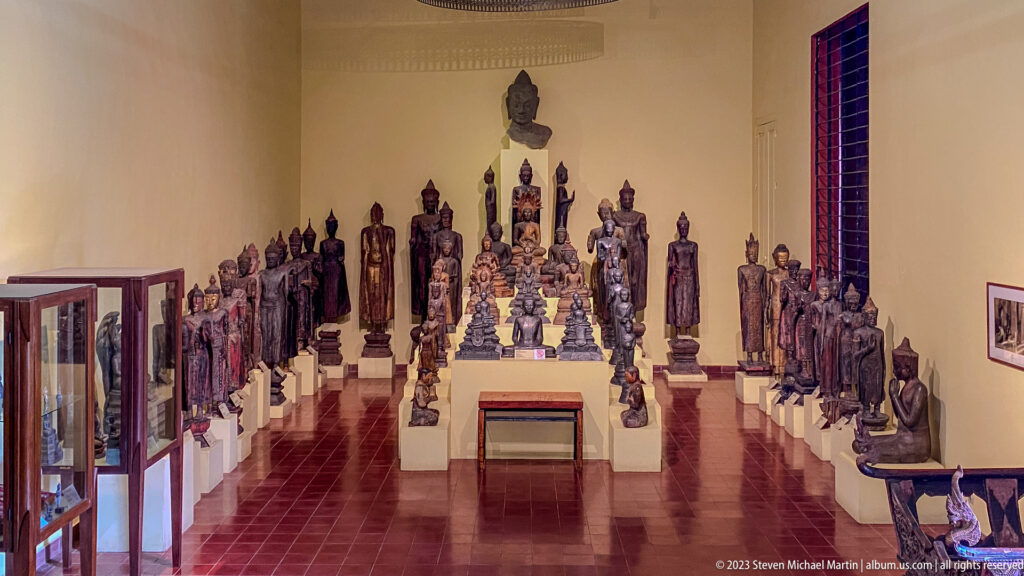 Wide gallery lined with rows of seated and standing Buddhist sculptures in bronze and stone.