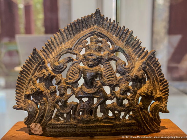 Openwork bronze devotional plaque with a central deity, attendants, and an arched frame.