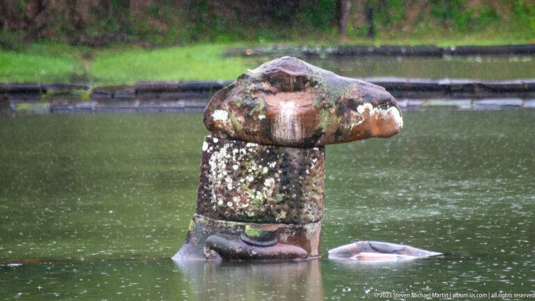 Weathered carved stone emerging from water.