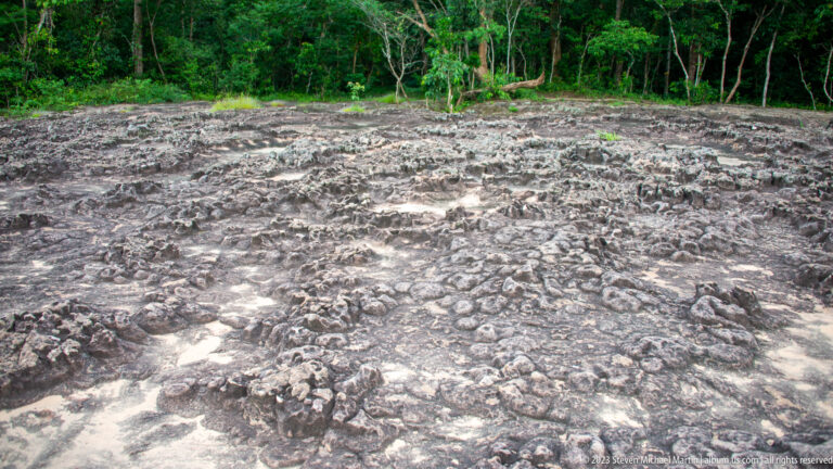 Close view of low weathered stone foundations and rubble across an exposed archaeological surface.