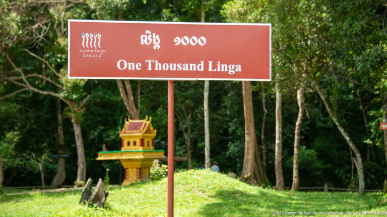 Red sign reading One Thousand Linga stands in a forest with a small shrine behind it.