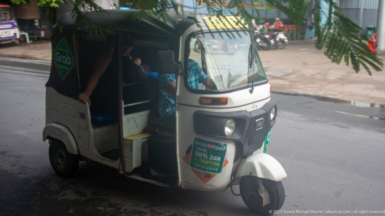 Gray Grab-branded motorized tuk-tuk stopped at the curb with passengers inside.
