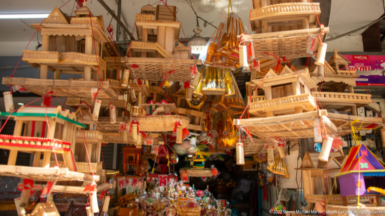 Dense market display of wooden and brightly painted miniature spirit houses with tiered roofs and columns.