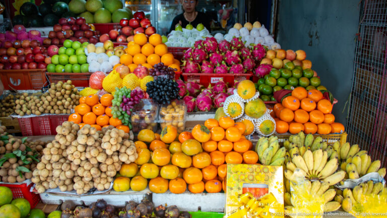 Colorful fruit stall packed with oranges, bananas, grapes, dragon fruit, apples, longans, and pomelos.
