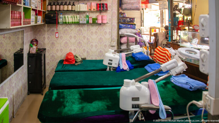 Small beauty salon room with two green-covered treatment beds, mirrors, towels, and cosmetic machines.