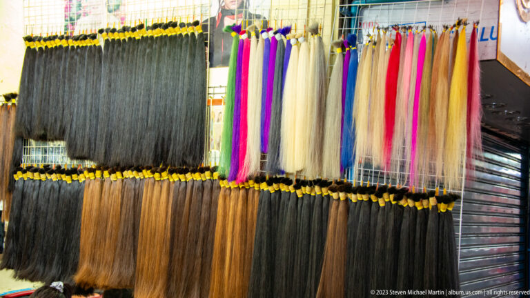 Rows of long synthetic hair extensions hanging in black, brown, blond, pink, purple, blue, and red.