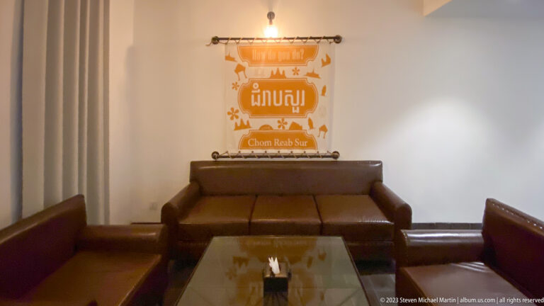 Brown leather lobby seating beneath an illuminated Chom Reab Sur greeting sign in Khmer and English.
