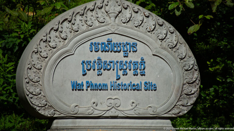 Carved stone sign with Khmer and English text reading Wat Phnom Historical Site.