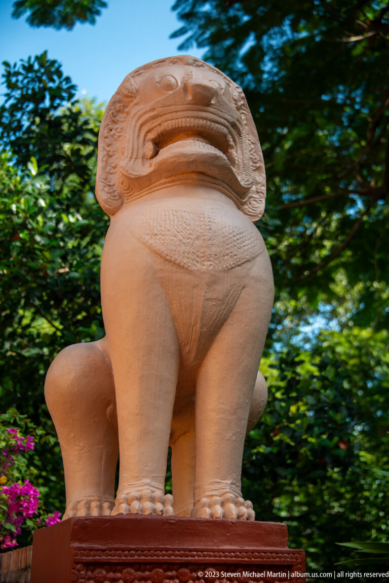 Terracotta-colored guardian lion sculpture standing on a pedestal against green trees.
