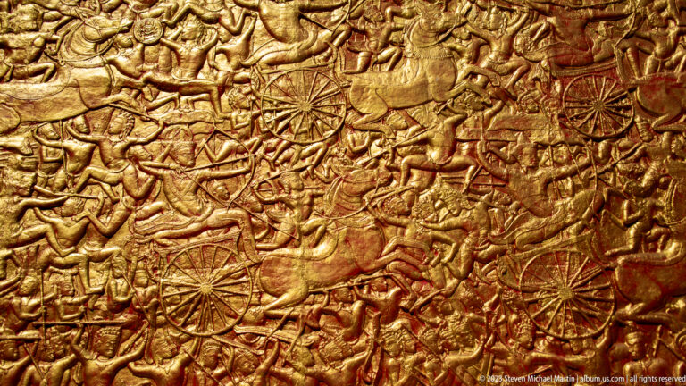 Close gilded relief packed with warriors, horses, elephants, chariots, and weapons in battle.