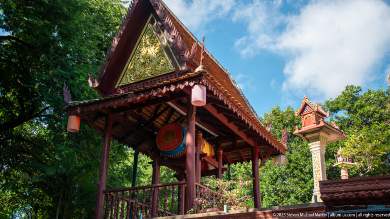 Open red wooden pavilion with steep gabled roof and suspended ceremonial drum or bell.