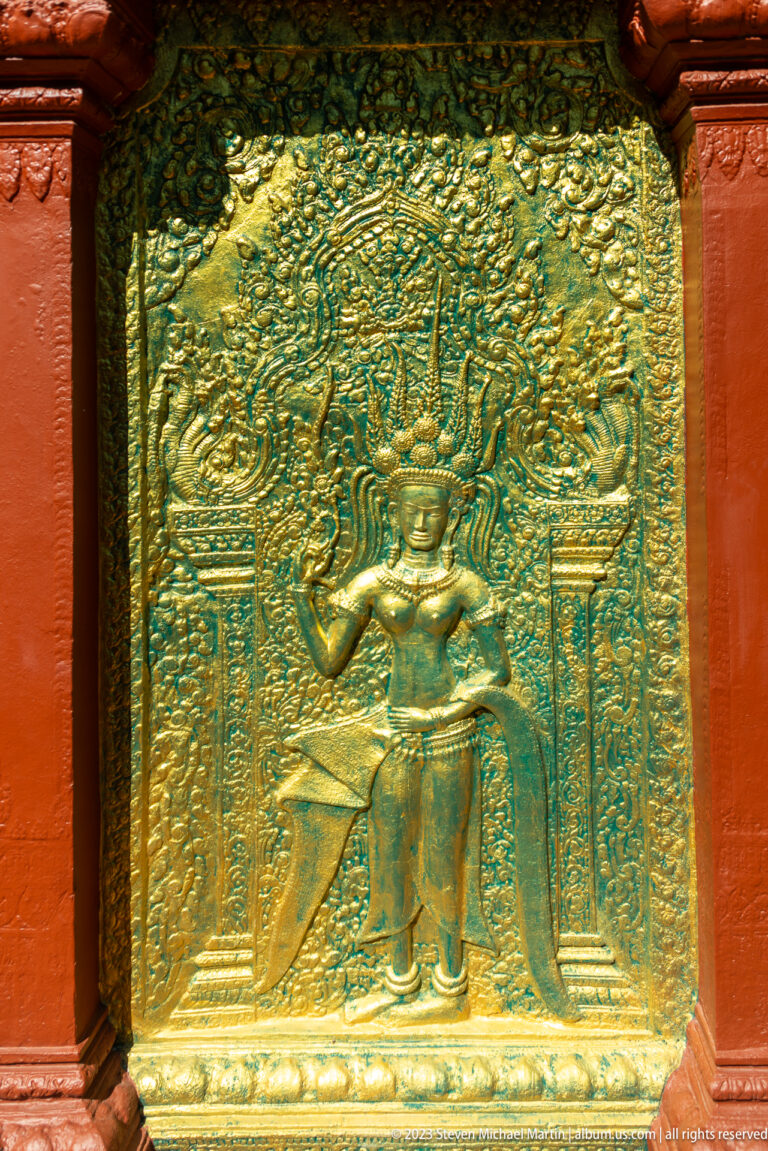 Gilded crowned figure with raised arms standing in an ornate niche framed by columns.