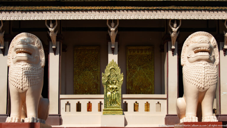 Two guardian lion sculptures flank gilded doors and a central relief at the Wat Phnom sanctuary entrance.