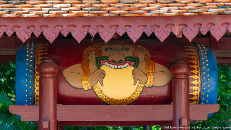 Close view of a painted ceremonial drum with a smiling face motif in a red wooden pavilion.