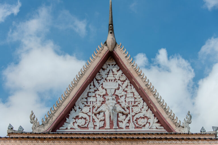 Triangular temple gable with white relief figures, vegetal ornament, and a tall central finial.