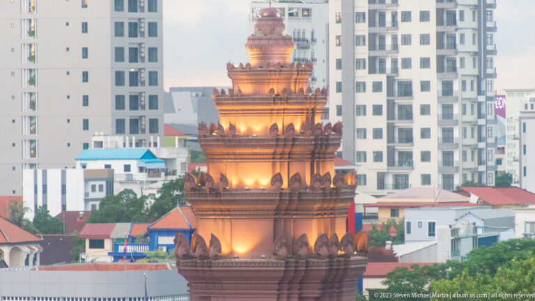 Close telephoto view of the illuminated upper tiers of Independence Monument against modern apartment buildings.