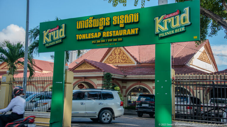 Green Tonlesap Restaurant gateway with Krud beer logos before an ornate red-roofed building.