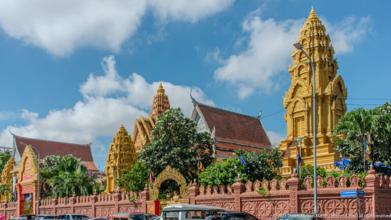 Ornate Buddhist temple complex with gilded towers, red roofs, carved walls, and pointed gables.