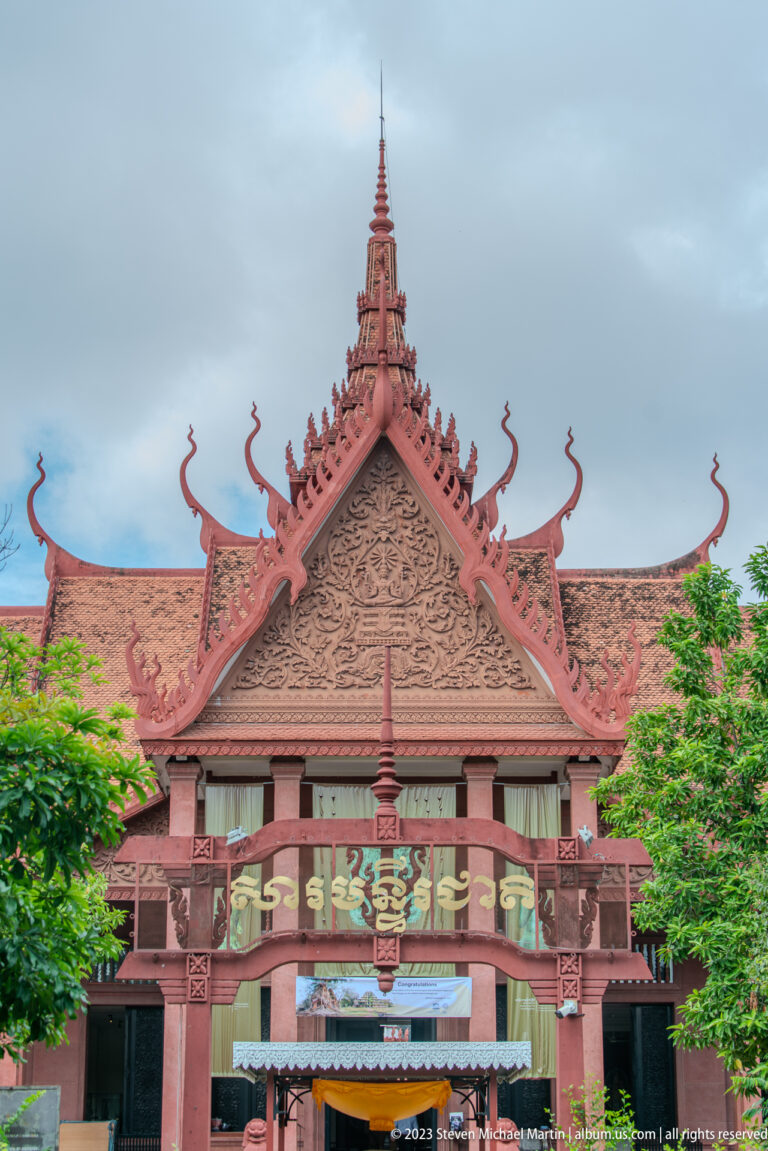 Reddish-brown Khmer-style façade with carved gable, curling roof finials, and central spire.