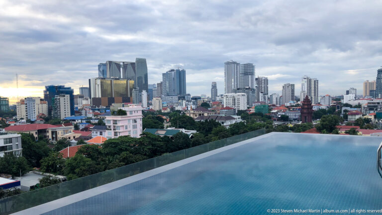Infinity pool overlooking a cluster of modern Phnom Penh towers, apartment blocks, and low green neighborhoods.