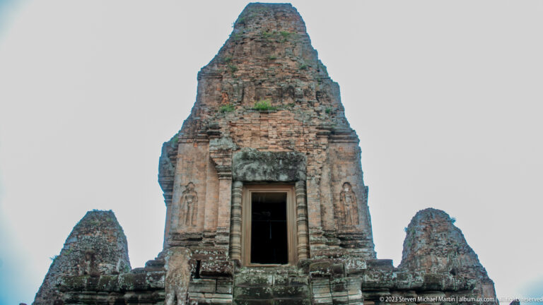 Low-angle view of a tall weathered brick tower with a pale sandstone doorway and smaller towers beside it.