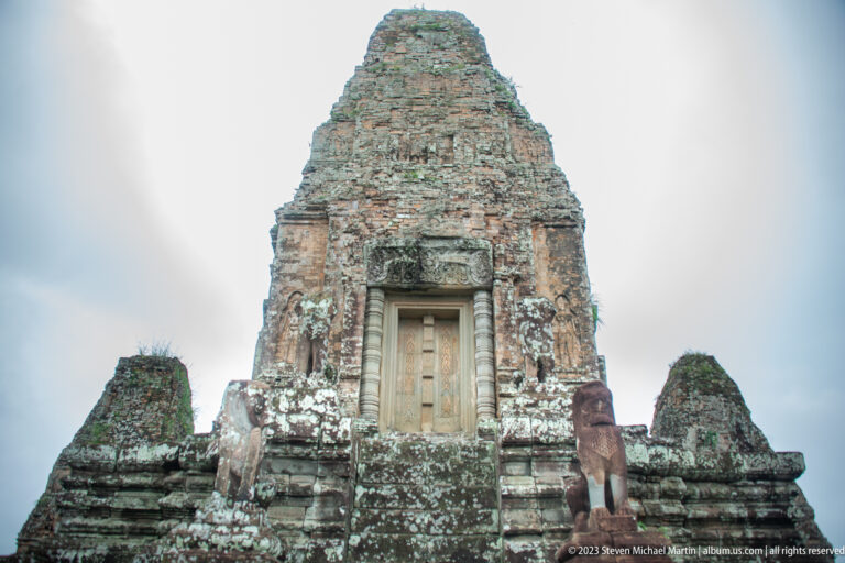 Brick sanctuary tower with a pale doorway and a carved elephant guardian on the terrace at right.
