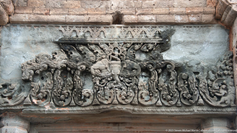 Sandstone lintel carved with a central seated figure and symmetrical scrolling ornament.