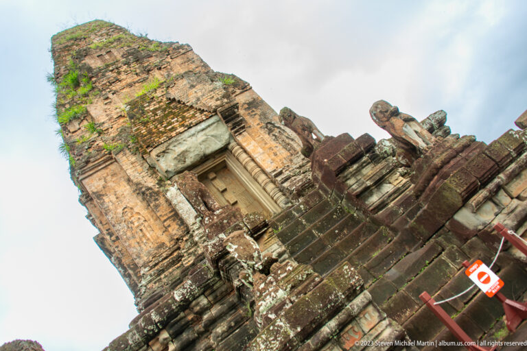 Steep upward view of a brick sanctuary tower and lion guardian above dark stone steps.