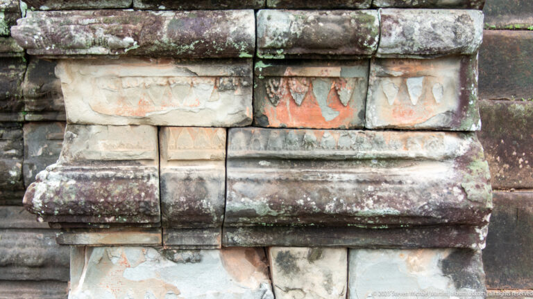 Close view of weathered masonry blocks with faded red and pale painted decorative traces.
