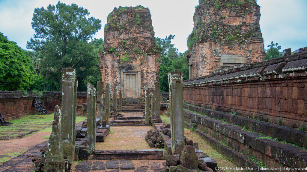 Stone-lined walkway at Pre Rup leading toward two tall weathered brick towers.