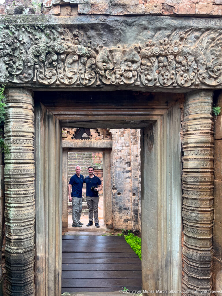 Two men standing beyond a carved sandstone doorway at the end of a straight temple passage.