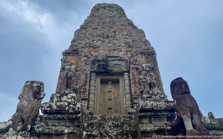 Low frontal view of a brick sanctuary tower with a sealed stone doorway and lion guardians on both sides.