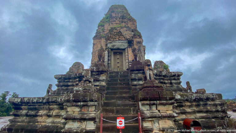 Frontal view of a brick sanctuary tower above steep steps with guardian figures and a visitor barrier.