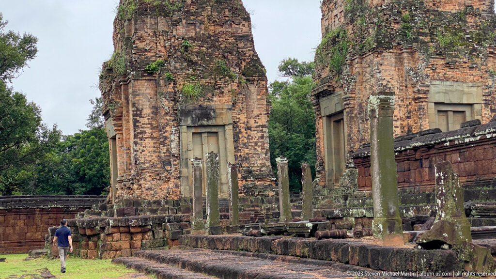 Visitor walking beside two tall brick towers and rows of stone posts in Pre Rup’s lower precinct.