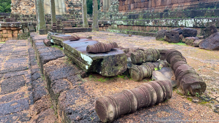 Carved cylindrical sandstone fragments and broken slabs resting on the temple pavement.