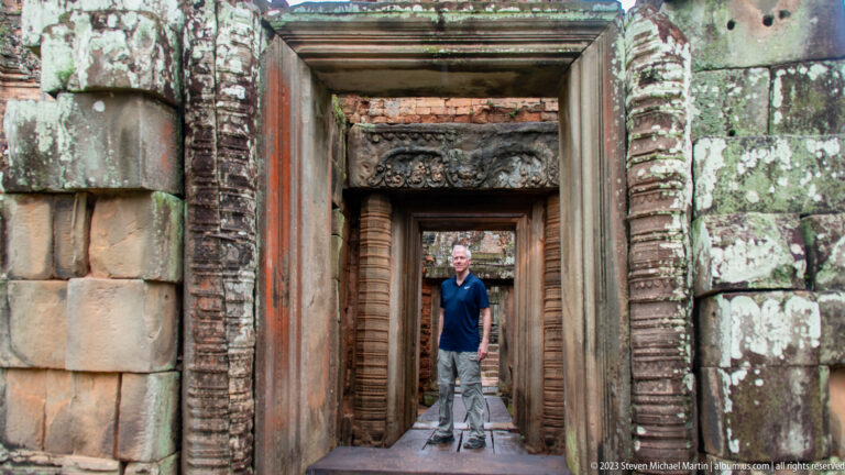 Man standing in a deeply recessed sequence of carved stone doorways at Pre Rup.