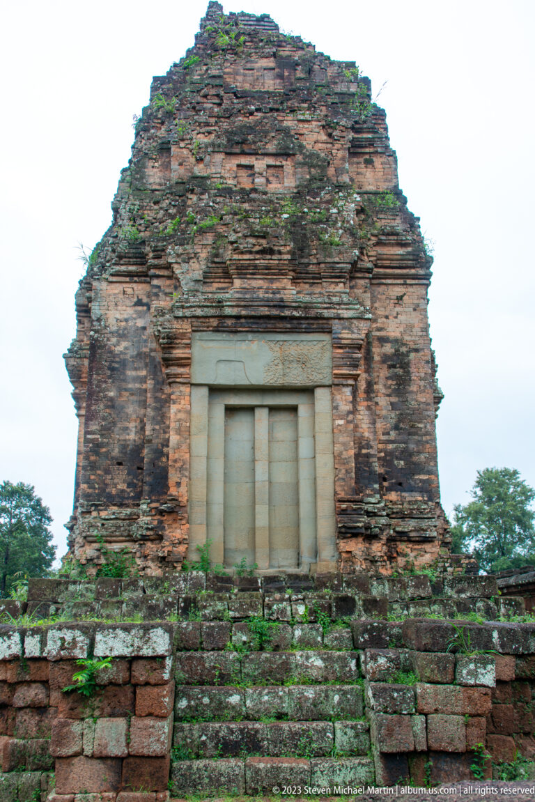Sealed pale stone doorway centered in a weathered brick tower above a short flight of steps.
