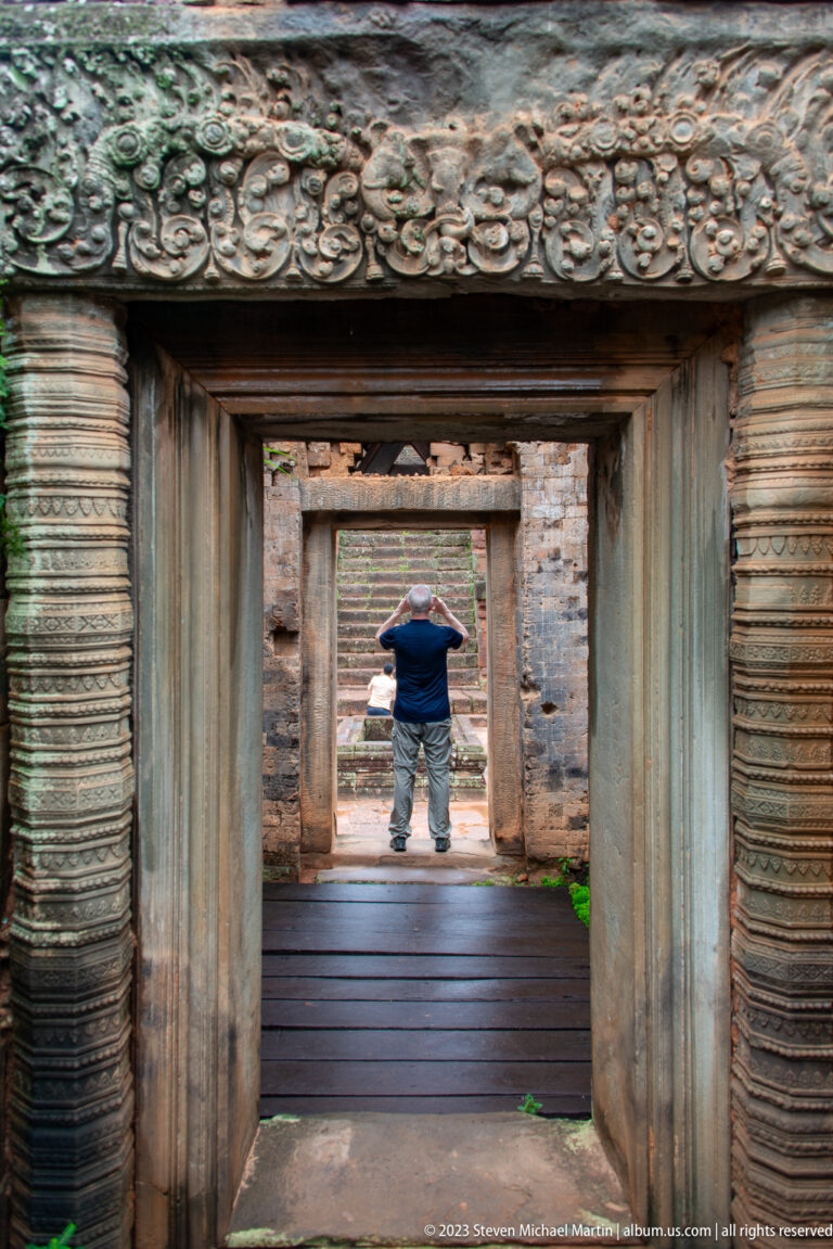 Aligned carved stone doorways at Pre Rup lead to a visitor standing beyond a wooden walkway.