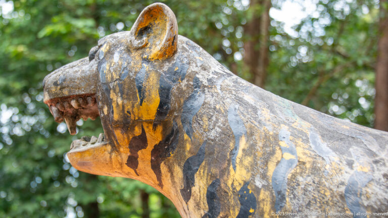 Weathered painted tiger statue with striped body and open mouth.