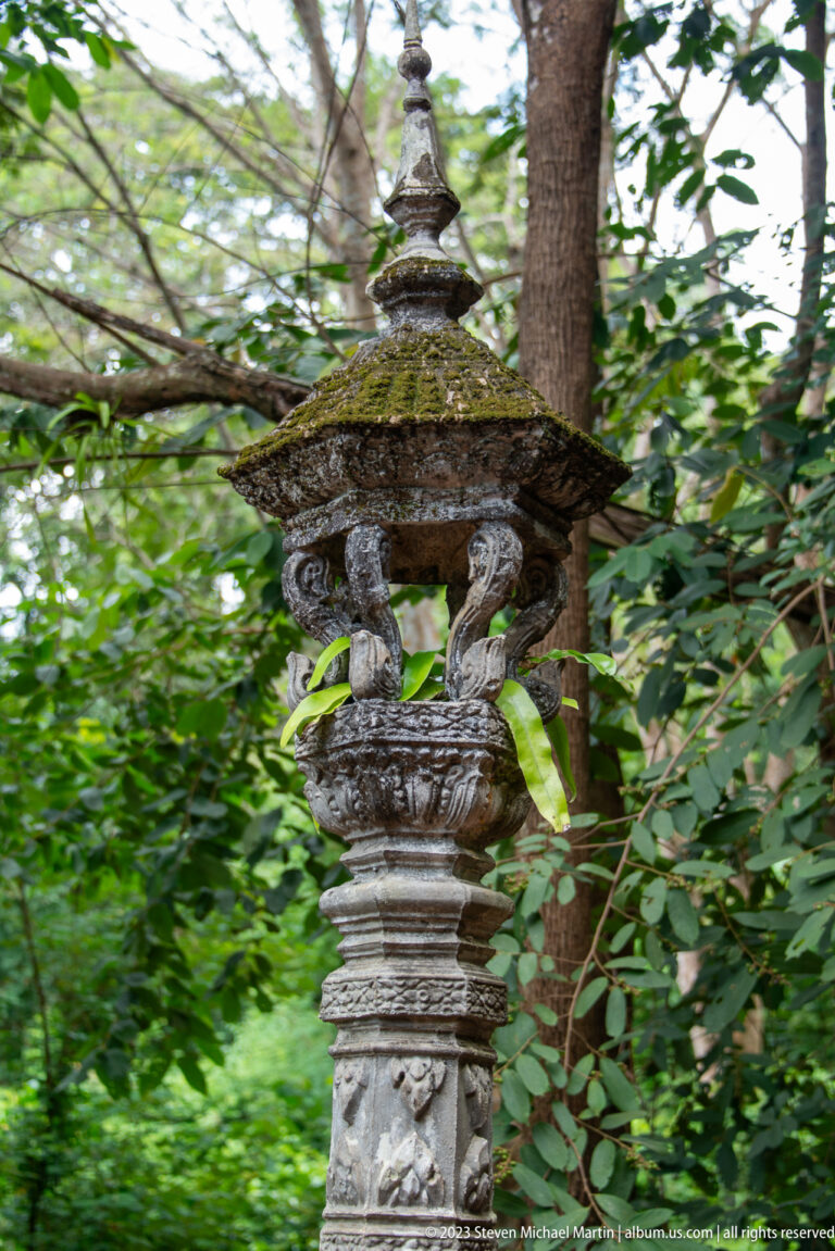 Moss-covered carved pedestal lantern standing among trees.