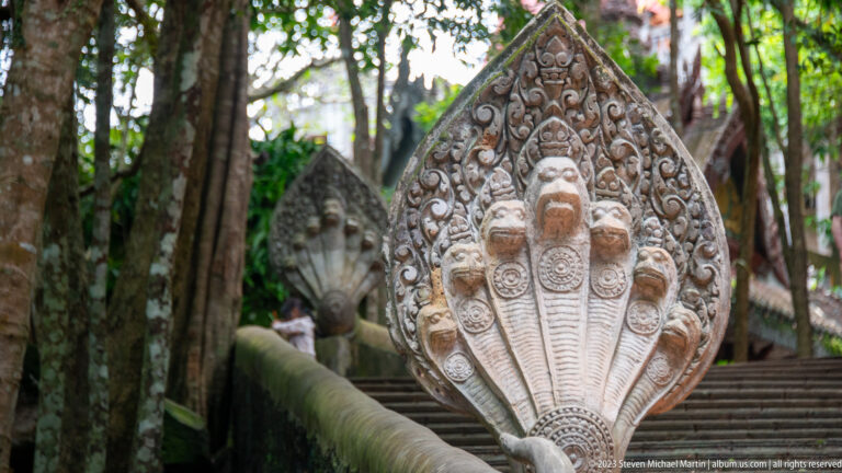 Five-headed naga finial beside a stairway ascending through trees.