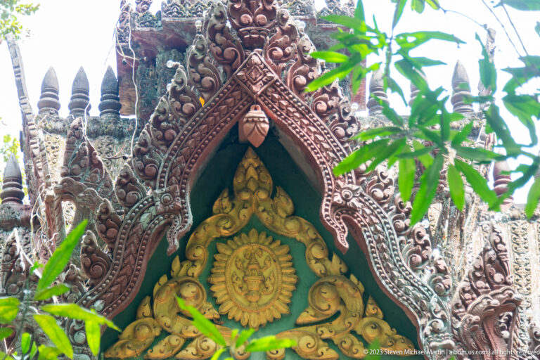 Ornate pointed temple gable with floral carving, small spires, and a golden central medallion.