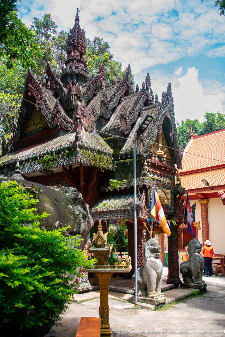 Oblique view of an ornate shrine with steep gables, guardian lions, and Buddhist flags.