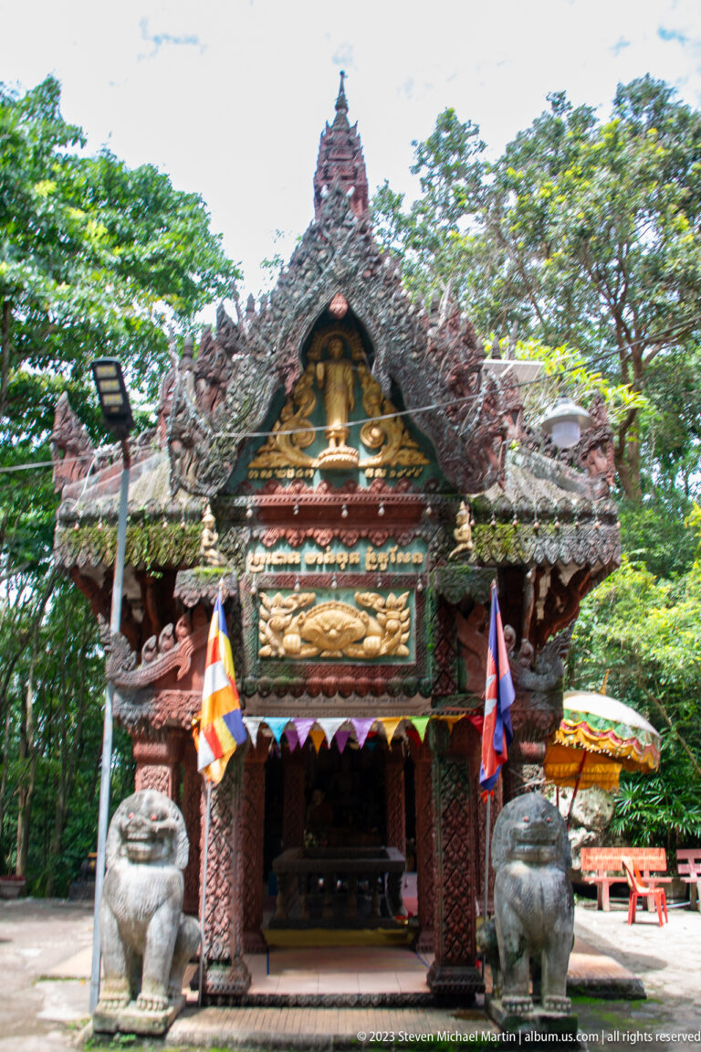 Frontal shrine façade with seated Buddha, guardian lions, and Buddhist flags.